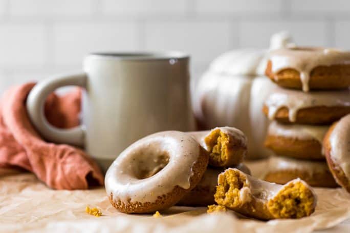 a stack of baked pumpkin donuts next to a cup of coffee