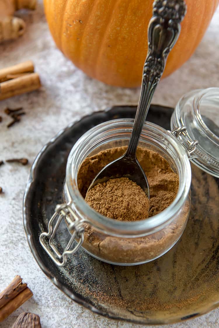 a small lidded jar on a black plate full of pumpkin spice mix, with a spoon inside