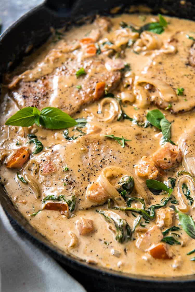 A skillet filled with Italian smothered pork chops and fresh herbs