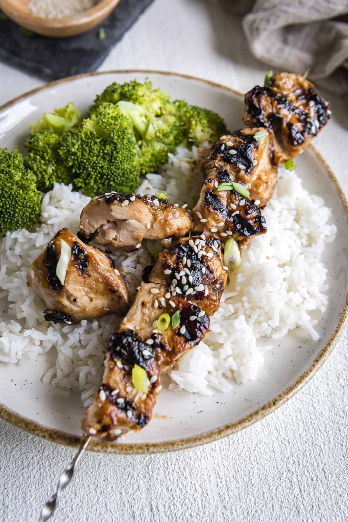 a grilled teriyaki chicken skewer on a plate of rice with broccoli