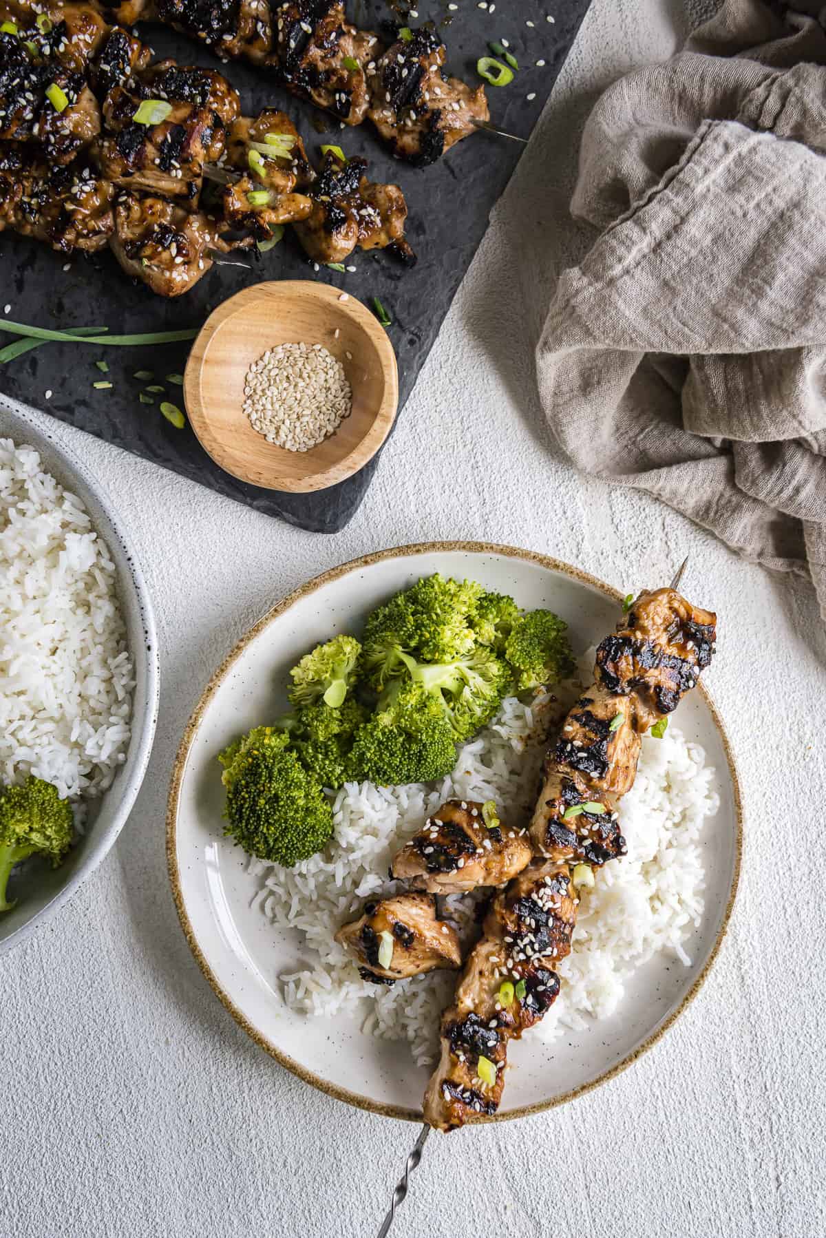 a grilled teriyaki chicken skewer on a plate of rice with broccoli