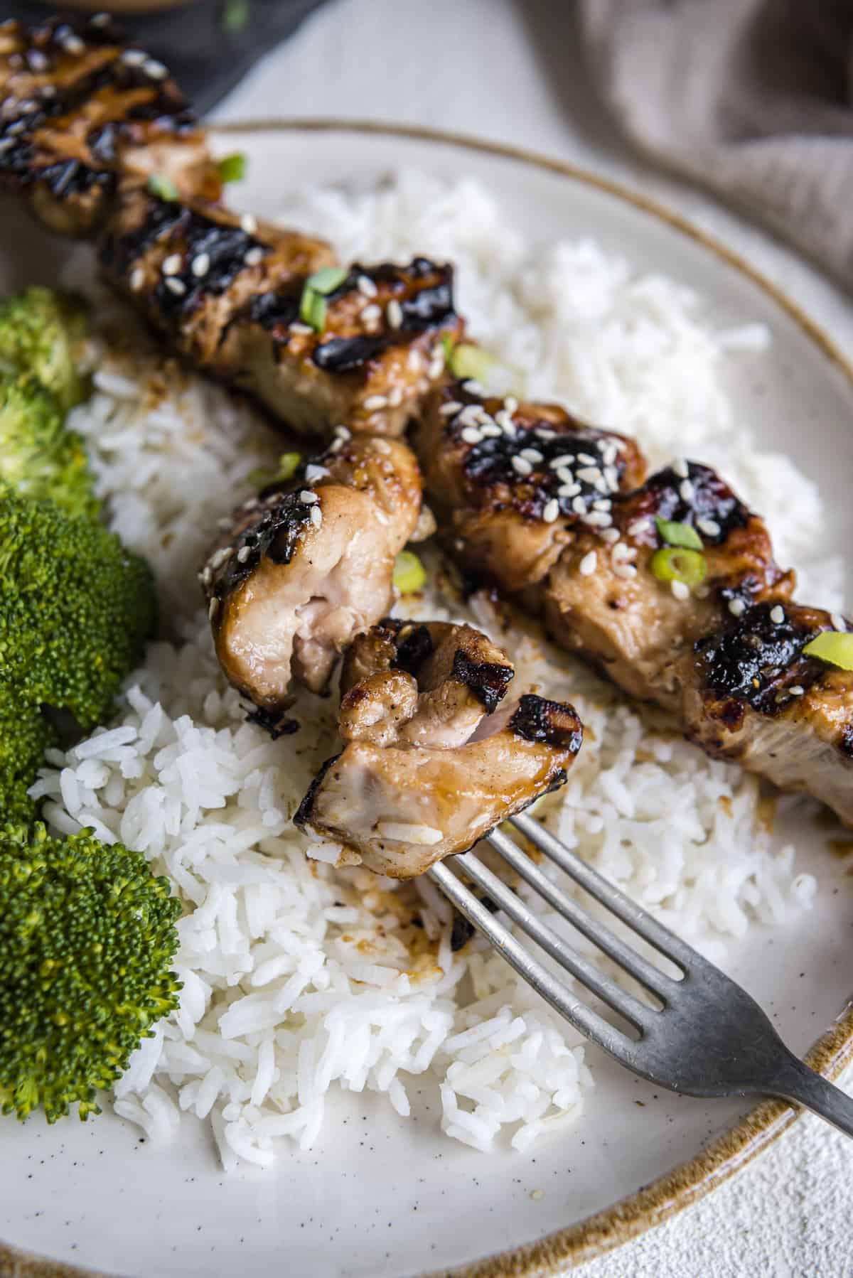 grilled teriyaki chicken skewers and a fork on a plate of rice with broccoli