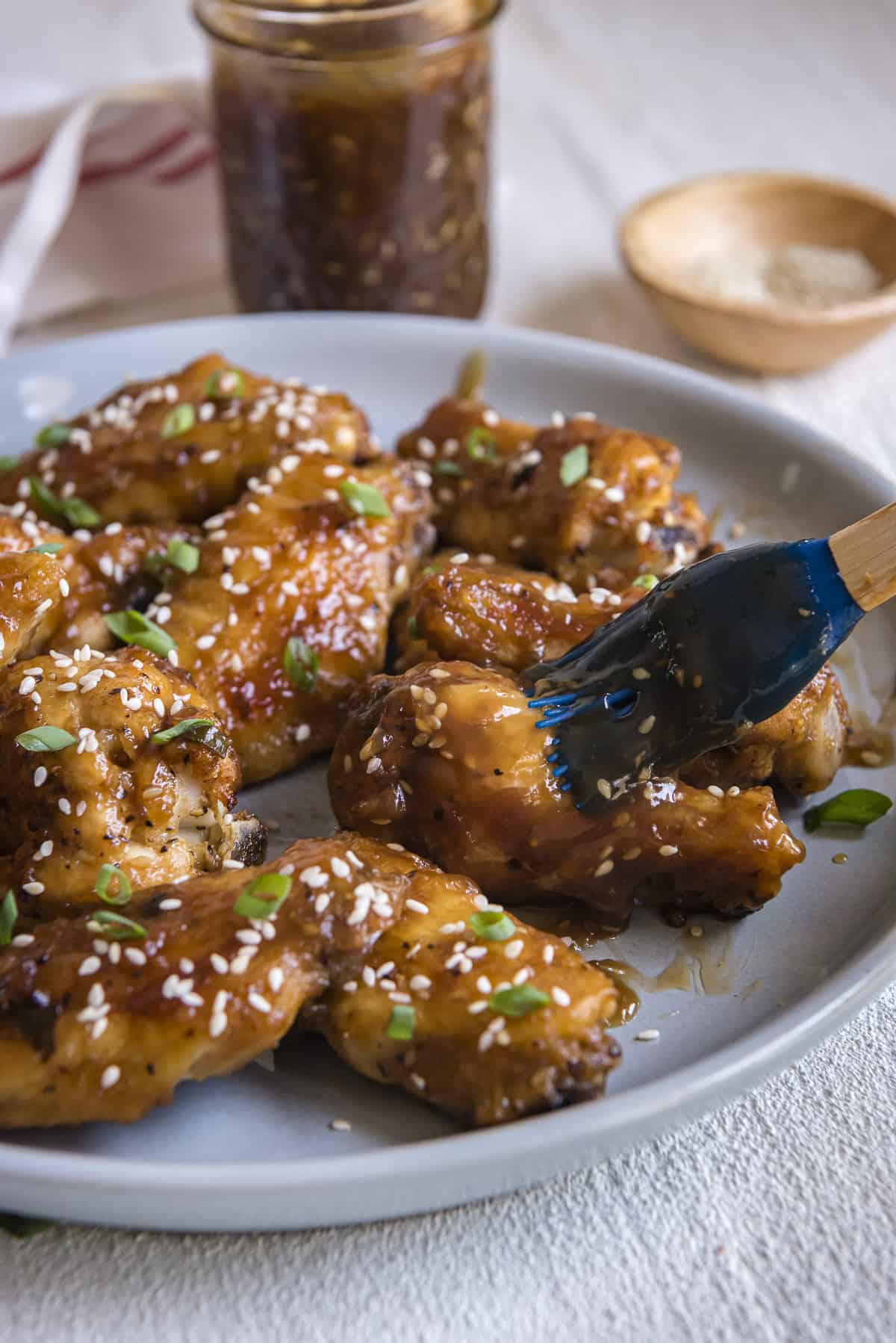 a plate of chicken wings being basted with teriyaki sauce