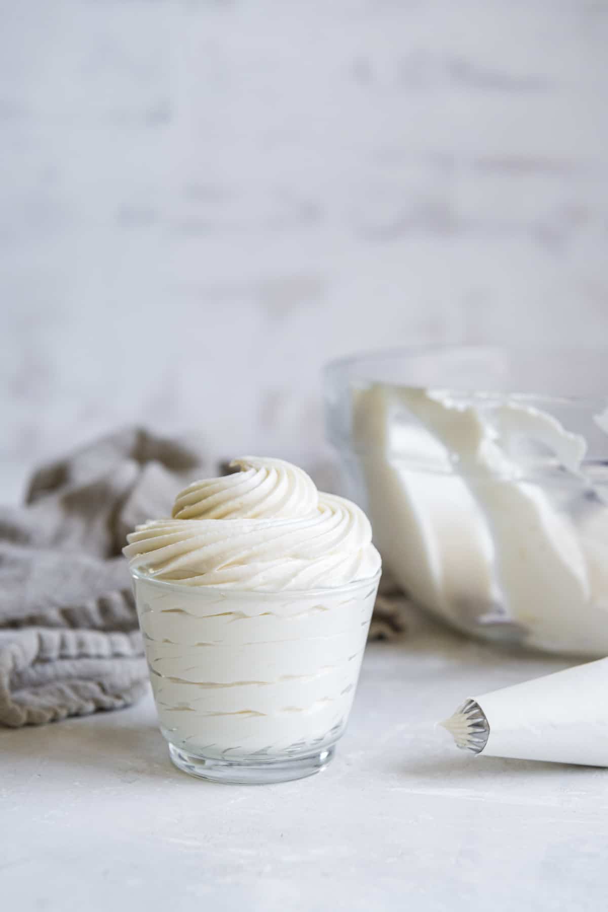 whipped cream cheese frosting piped into a small glass container with a piping bag nearby