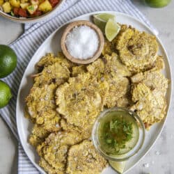 air fried tostones on a white platter with bowls of salt, garlic oil, and salsa