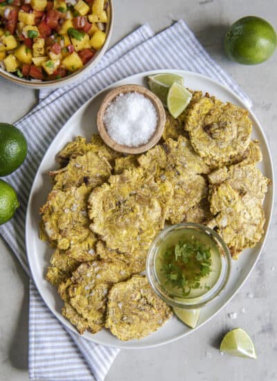 air fried tostones on a white platter with bowls of salt, garlic oil, and salsa