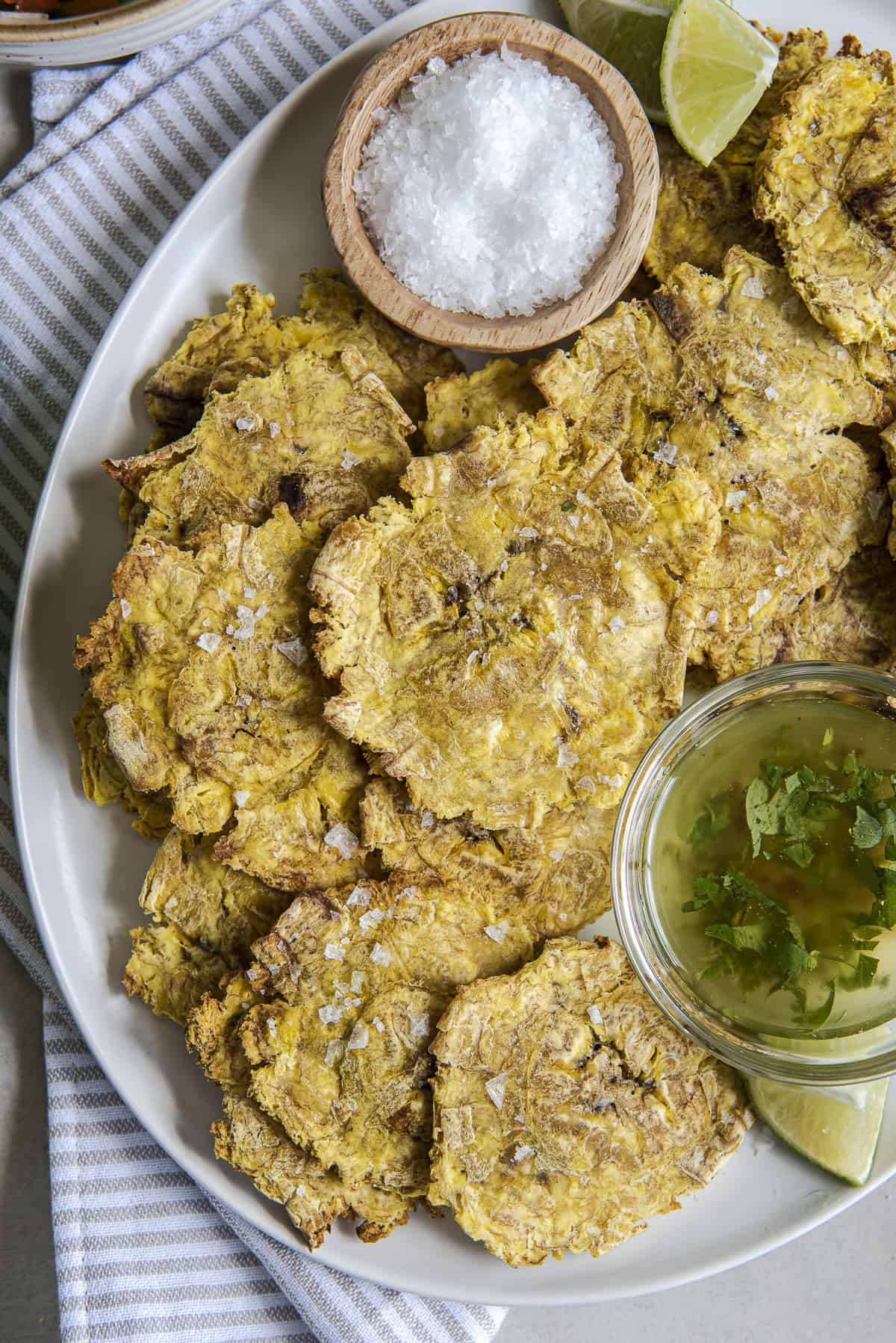 air fried tostones on a white platter with bowls of salt and garlic oil