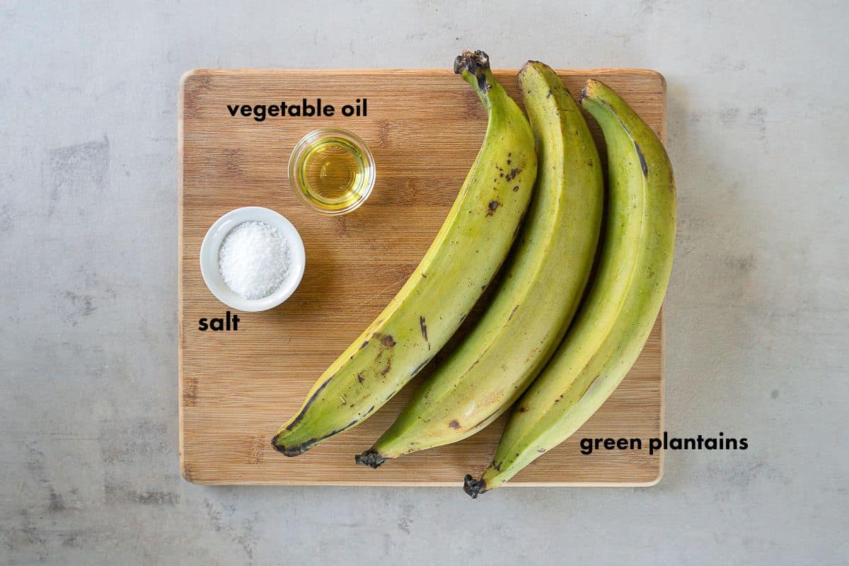 ingredients for air fryer tostones on a cutting board - green plantains, salt, avocado oil