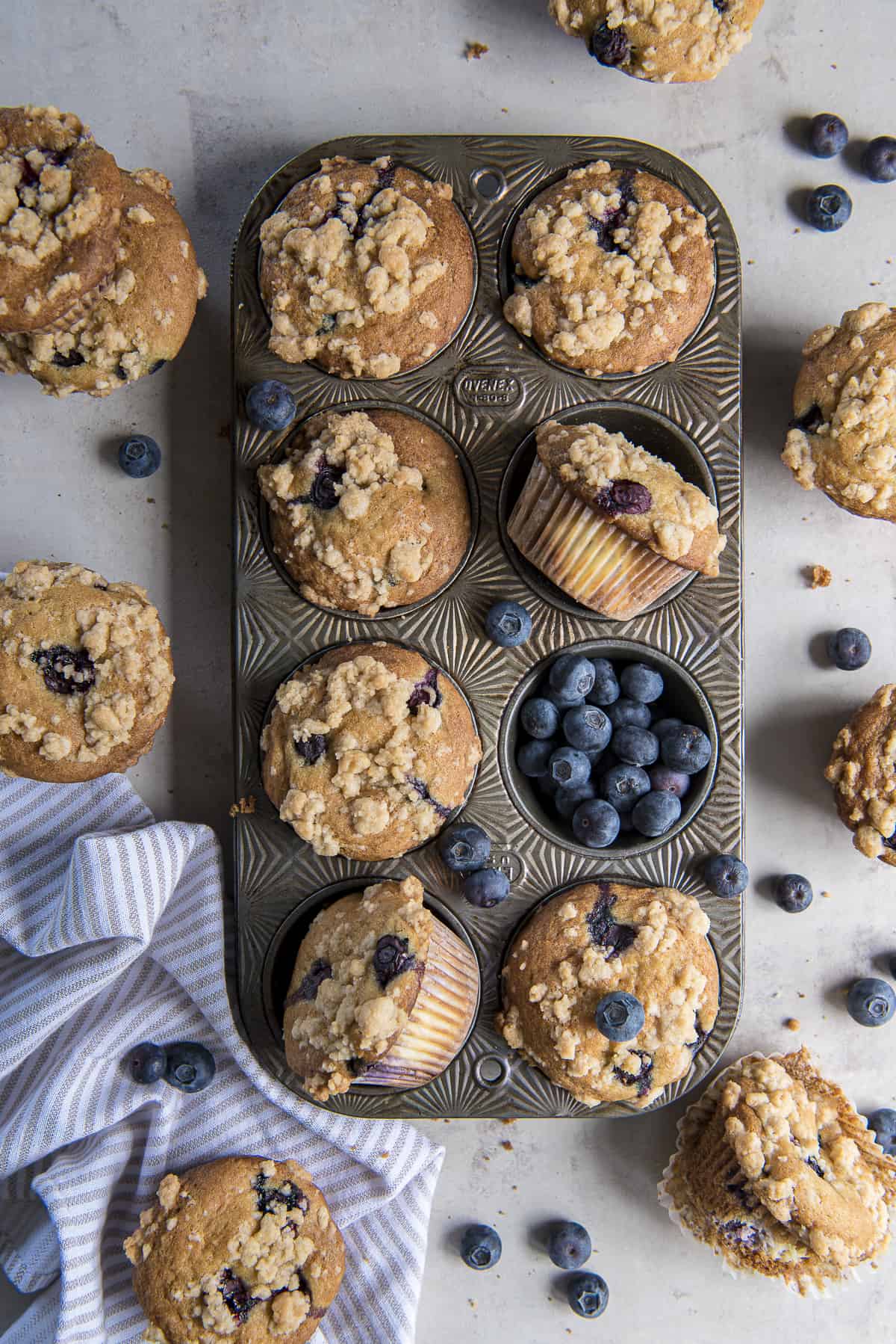 a vintage muffin pan full of blueberry cheesecake muffins, with blueberries scattered around.