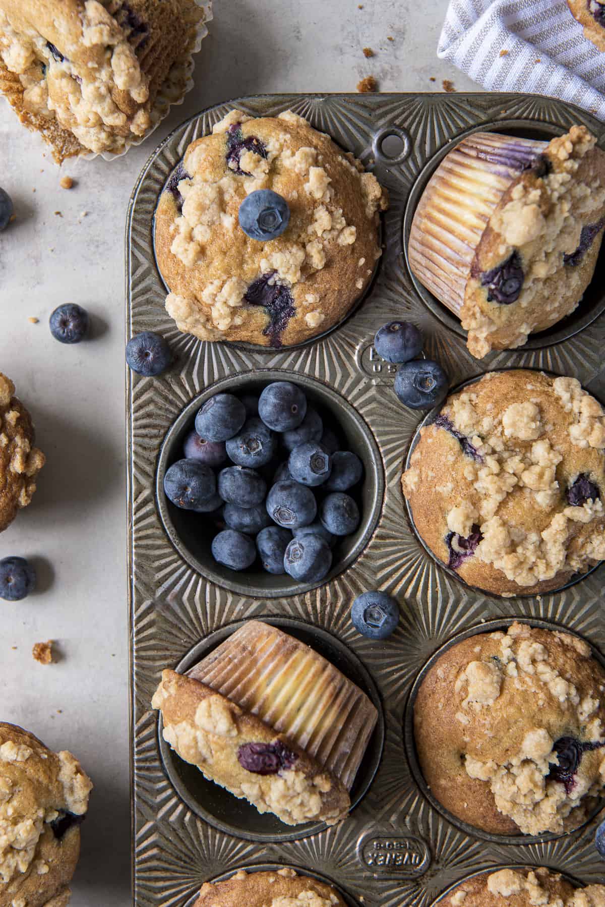 a vintage muffin pan full of blueberry cream cheese muffins, with one cup full of blueberries