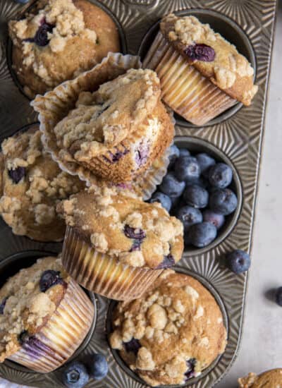 blueberry cheesecake muffins in a vintage muffin tin with blueberries scattered around.