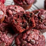 a red velvet muffins with a bite taken out of it sitting on a pile of more muffins
