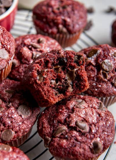 a red velvet muffins with a bite taken out of it sitting on a pile of more muffins