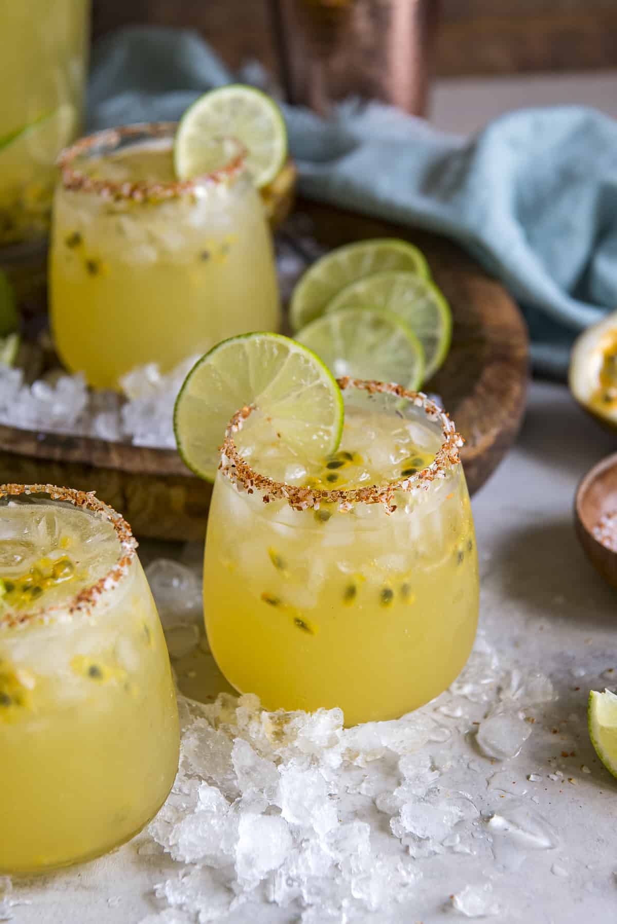 several glasses of passion fruit margaritas surrounded by ice and fresh lime