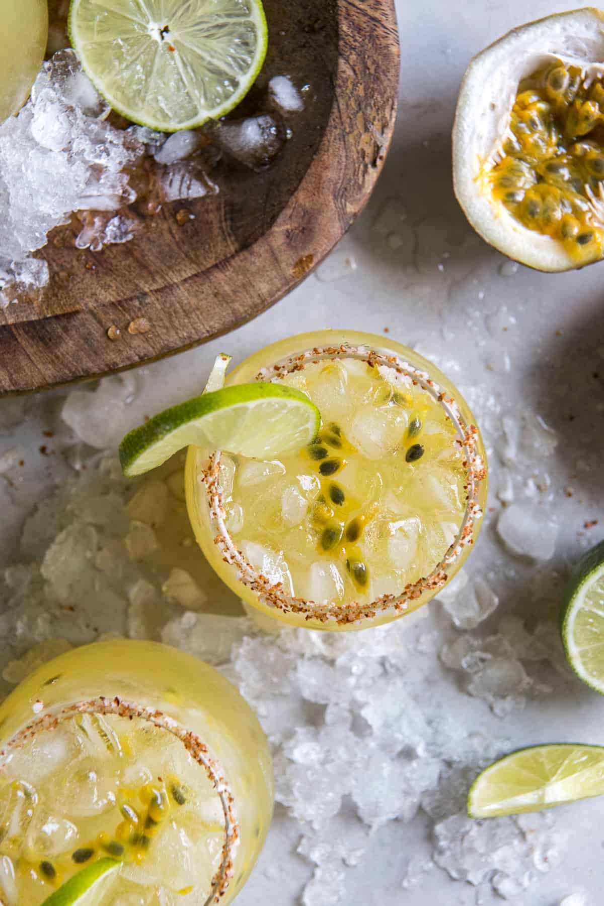 several glasses of passion fruit margaritas surrounded by ice and fresh lime