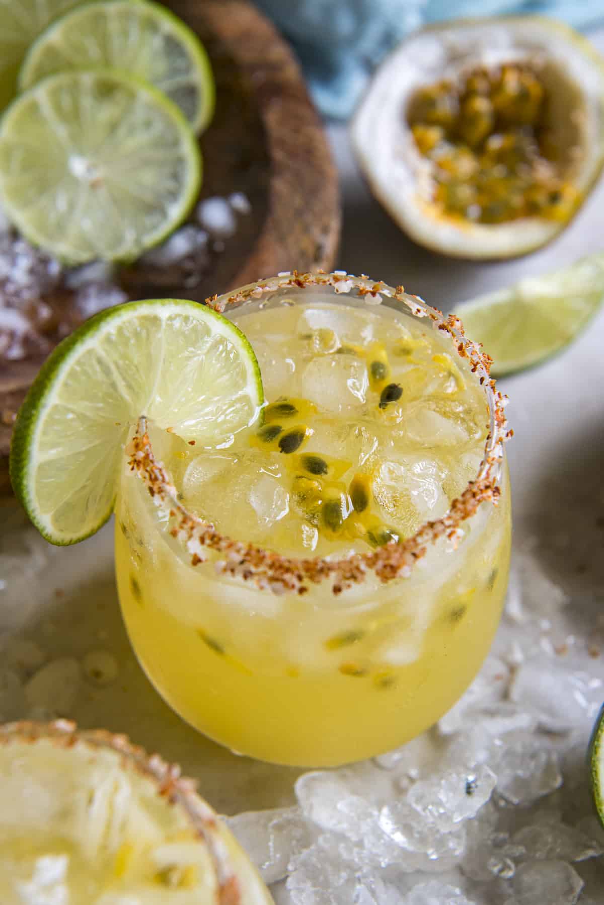 a glass of passion fruit margaritas surrounded by ice and fresh lime