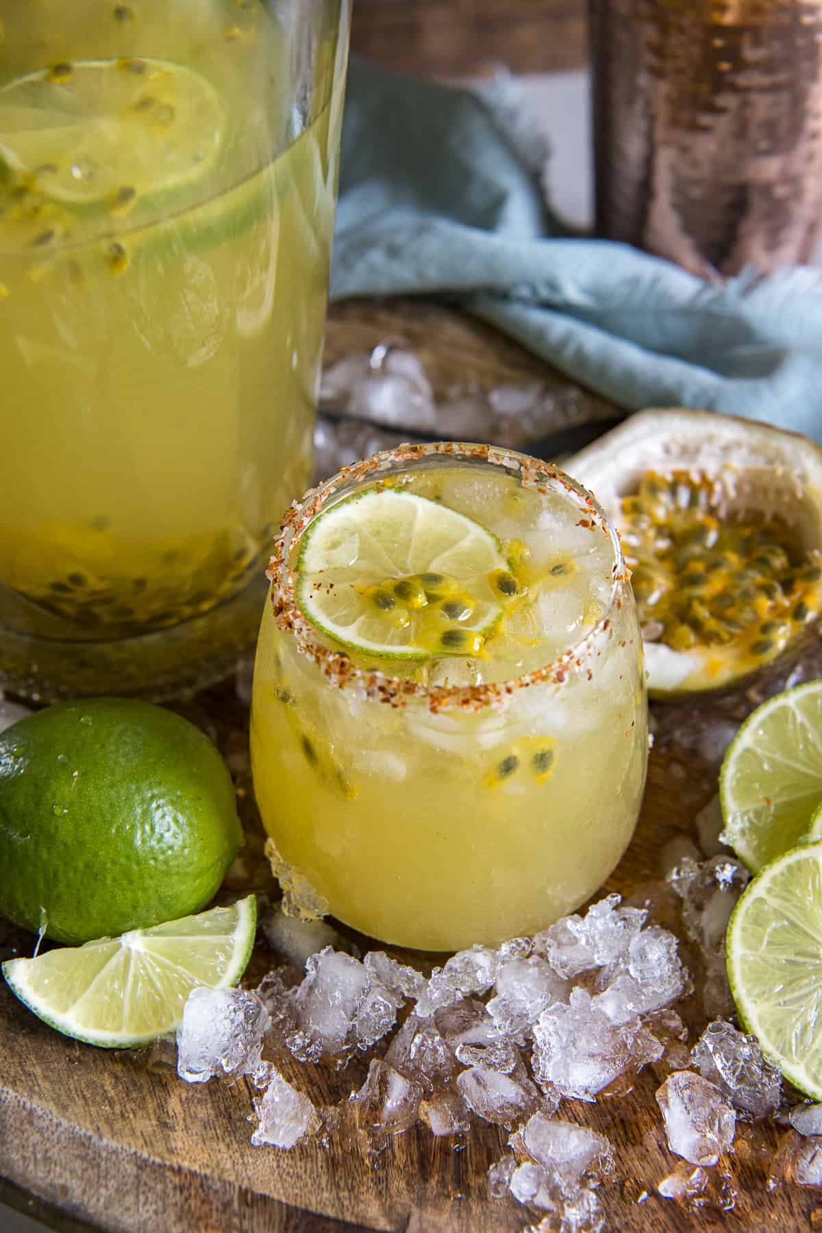 a glass of passion fruit margarita on a wooden tray with a pitcher of margaritas behind