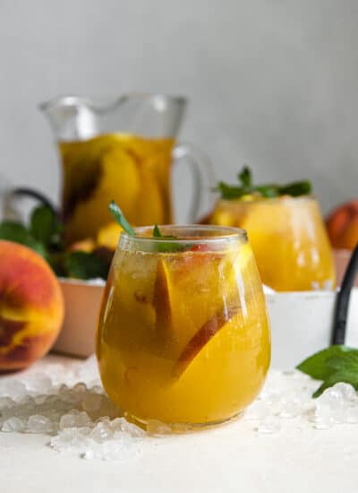 white peach sangria in a wine glass with a pitcher and peaches scattered in the background