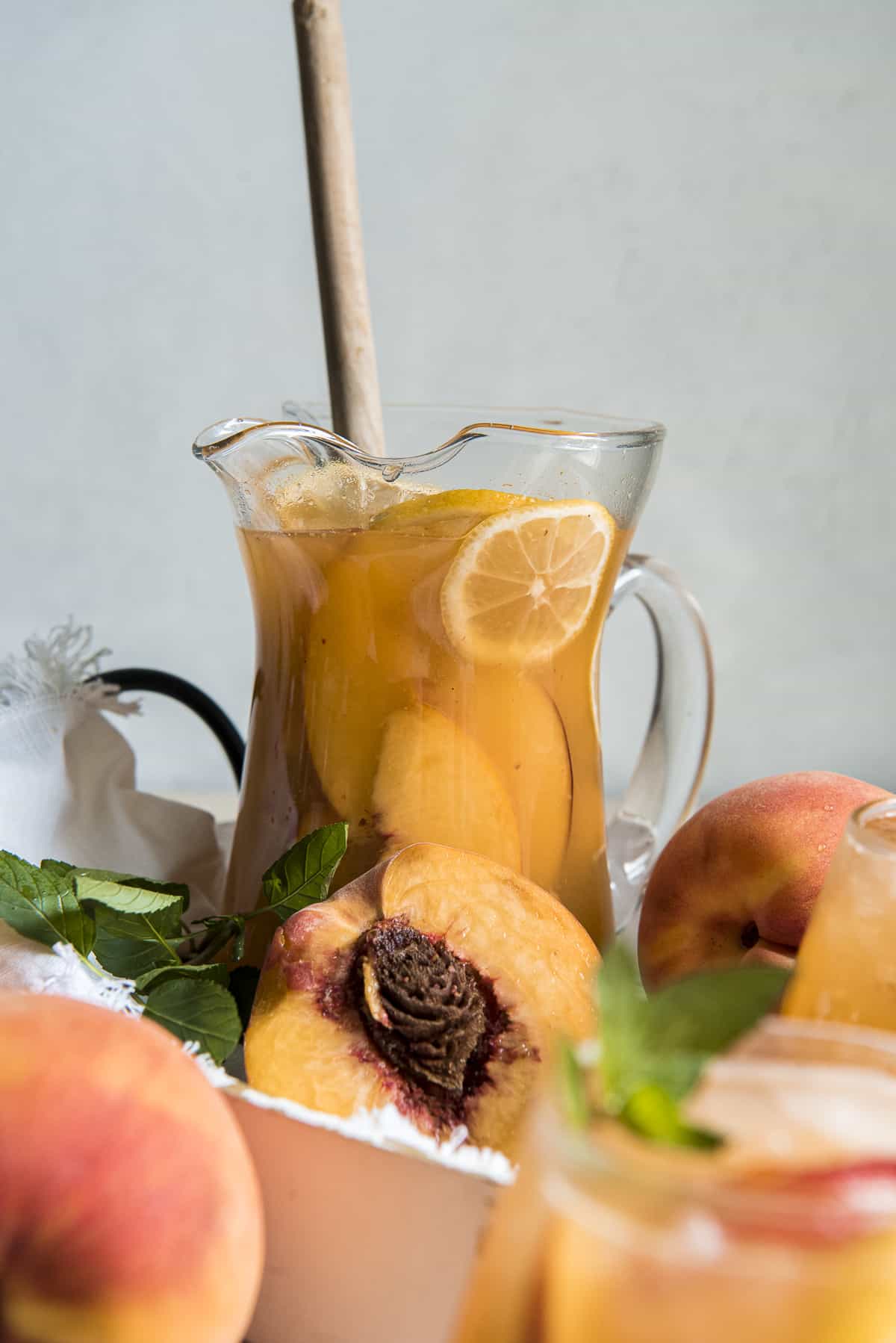 a pitcher of peach sangria on a white platter with peaches around it