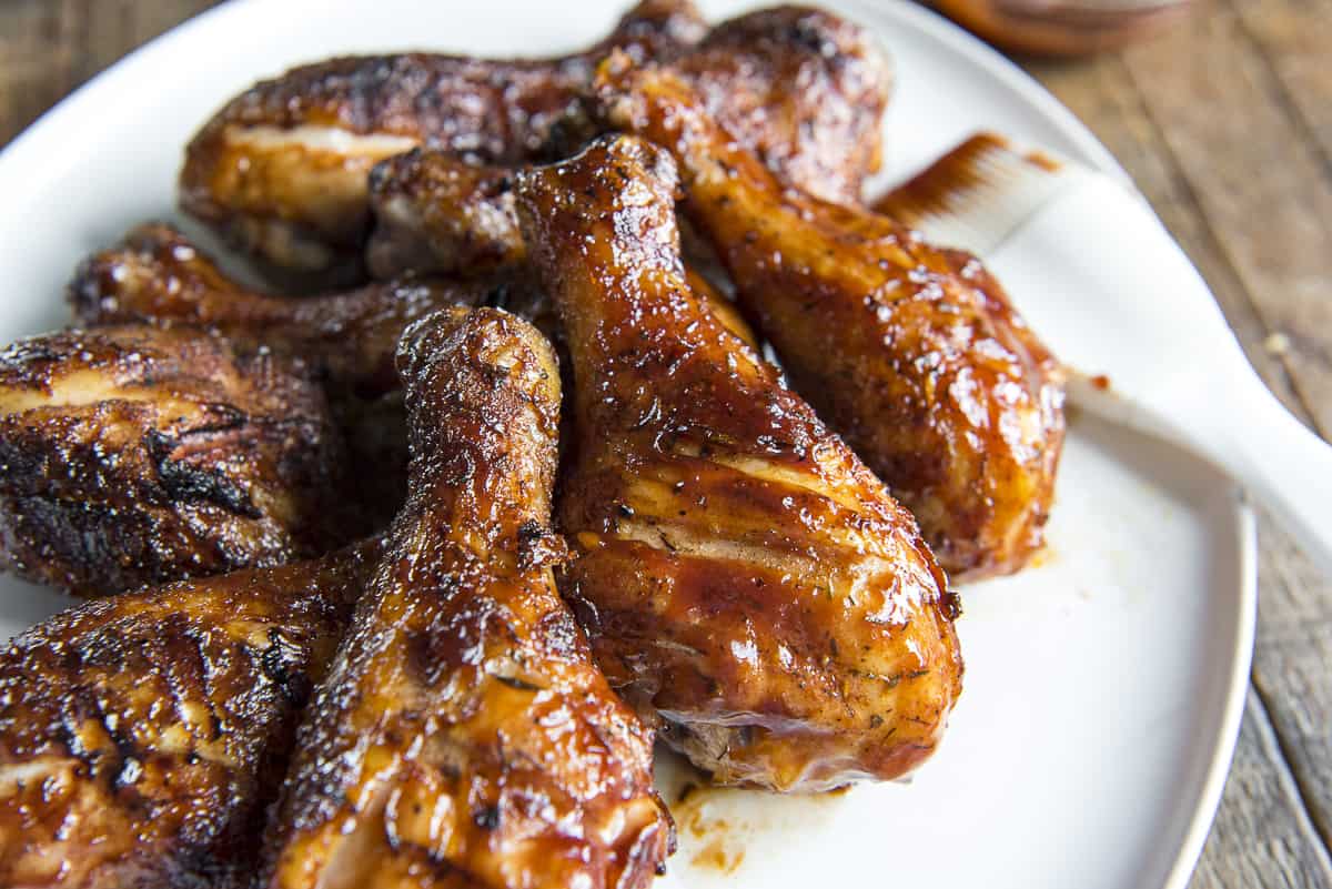 a white plate full of smoked bbq chicken legs with a basting brush in the background