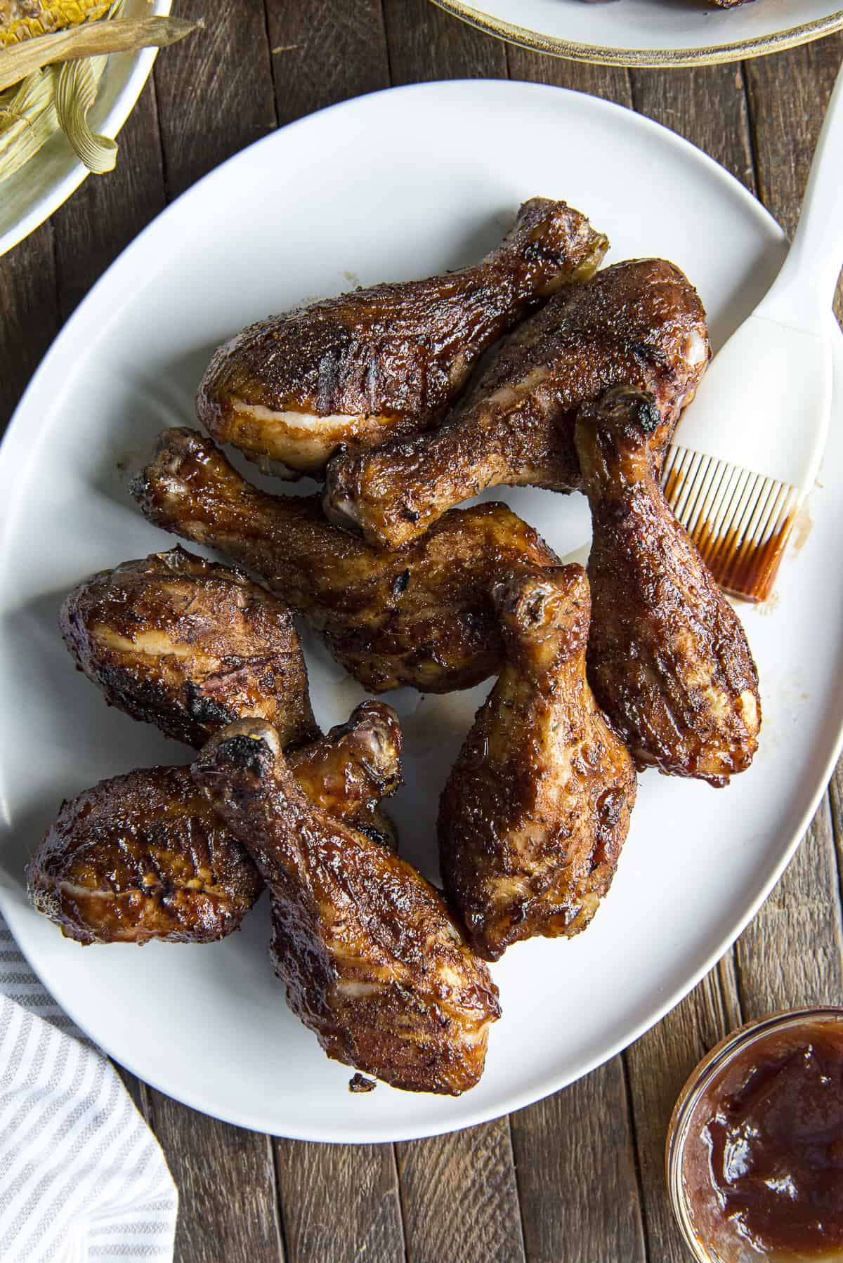 a white plate fill of bbq chicken legs with a basting brush in the background