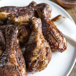 a white plate of smoked chicken legs with a small bowl of bbq sauce in the background