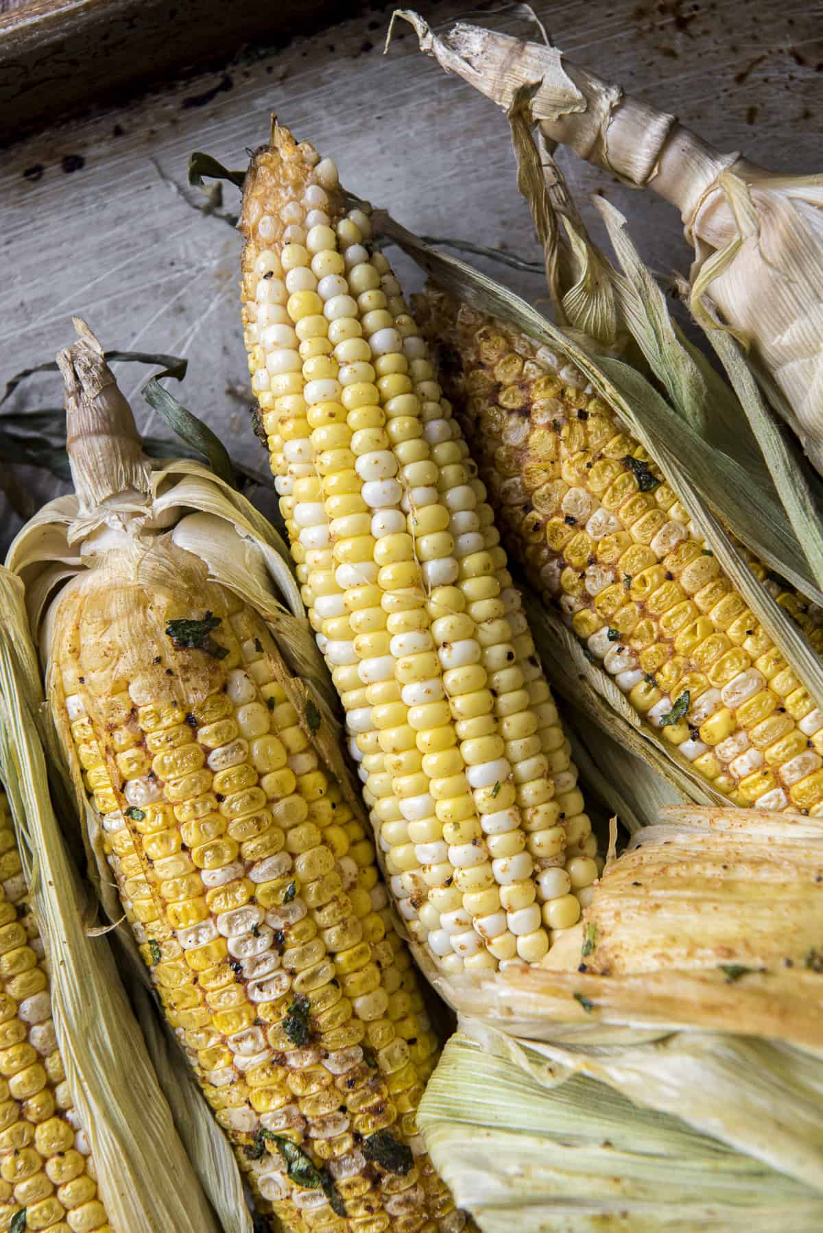 ears of smoked corn on the cob in their husks on a baking sheet