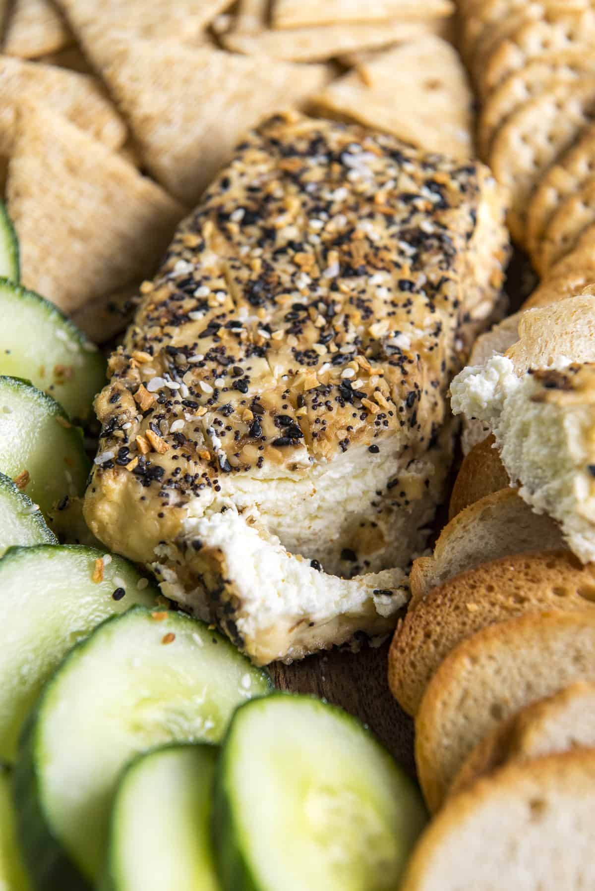 a block of everything smoked cream cheese with a chunk cut off surrounded by crackers and cucumbers