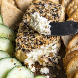 a block of smoked cream cheese with a spreader surrounded by crackers and cucumbers