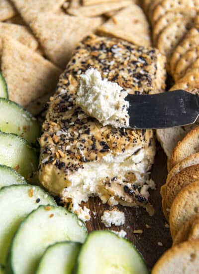 a block of smoked cream cheese with a spreader surrounded by crackers and cucumbers