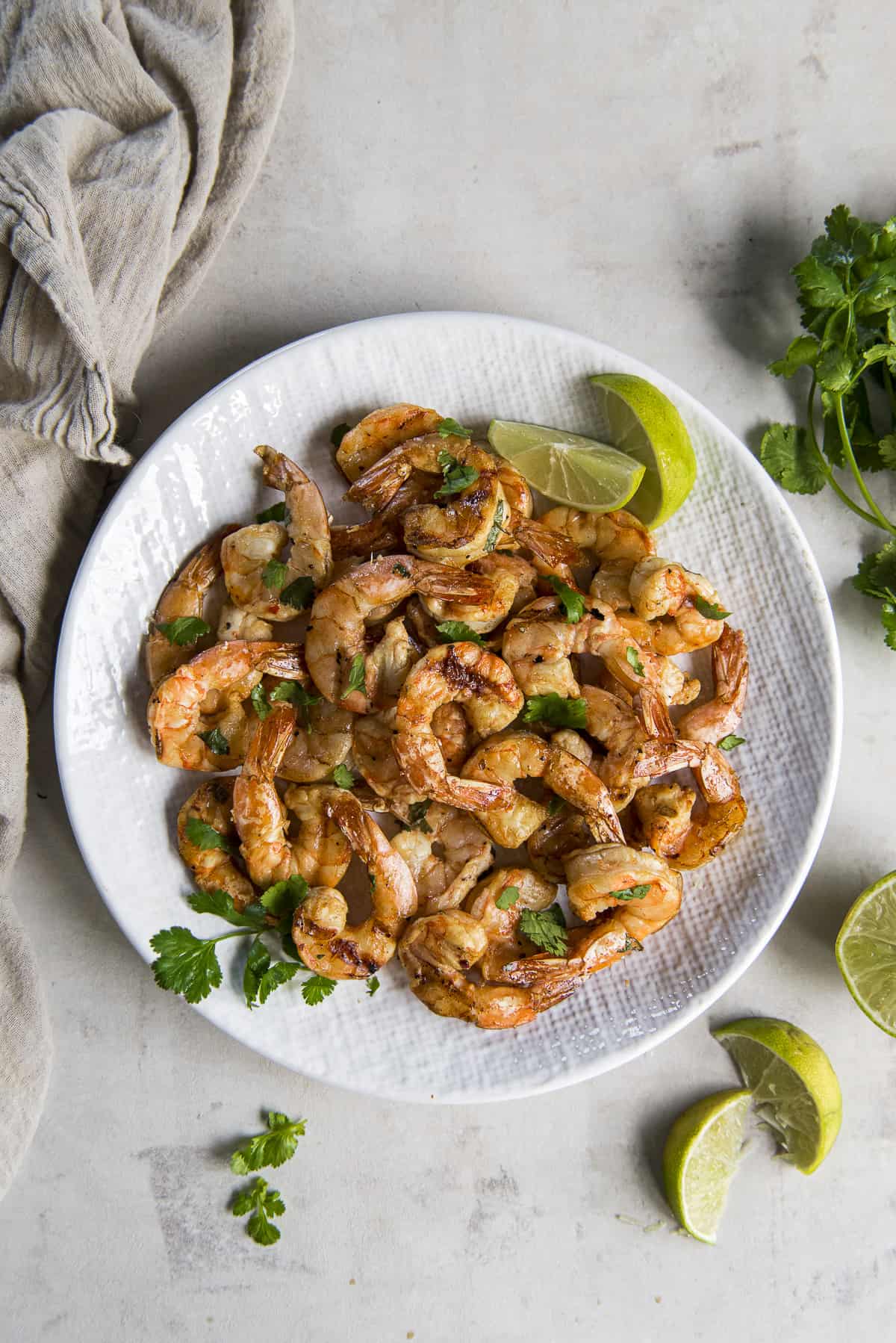 Tequila lime smoked shrimp on a white plate with lime wedges and cilantro