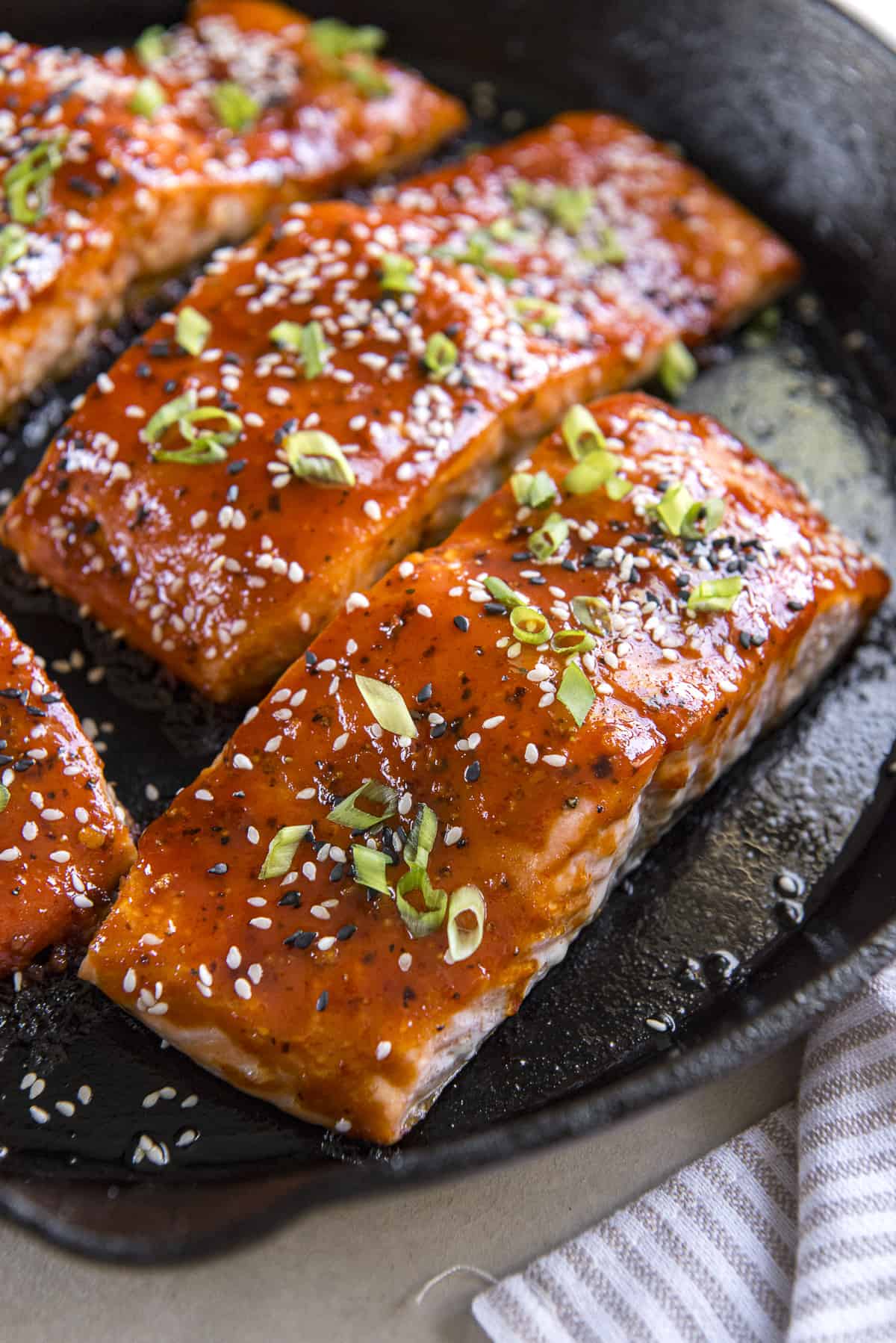 Korean Salmon fillets in a skillet with sesame seeds and green onions.