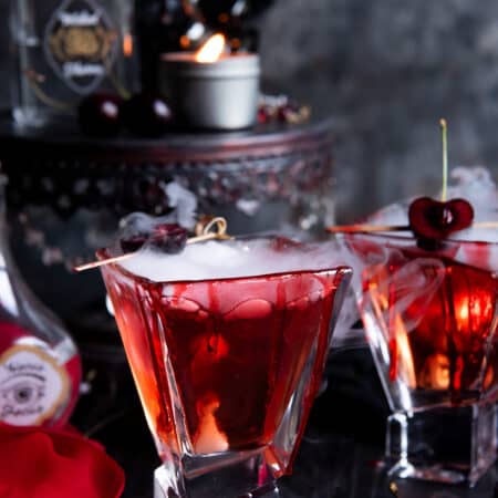 Two vampire's kiss cocktail with dry ice and cherries on them.